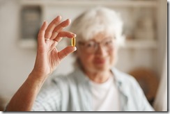 Food, nutrition, diet and health concept. Close up shot of elderly woman's hand holding fish oil or omega-3 polyunsaturated fatty acid supplement in shape of capsule, going to take one during lunch