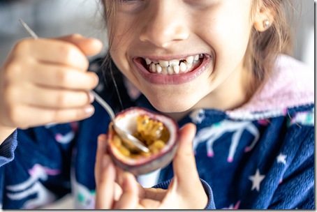 Little girl eats passion fruit, mouth close-up.
